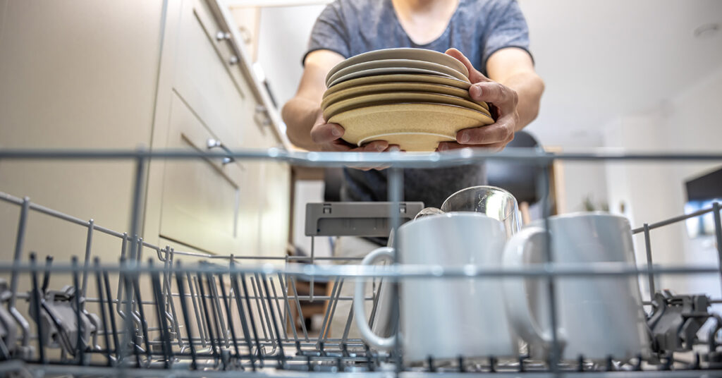 The man takes the washed dishes from the dishwasher.